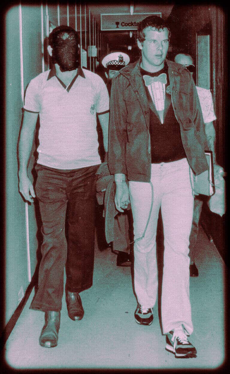 Vintage tinted photo of a young man walking with police officers indoors.