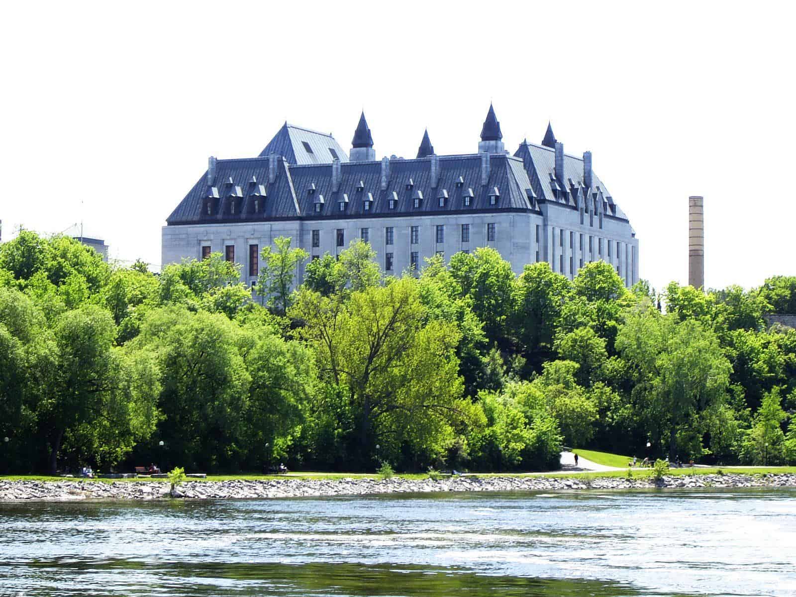 The Supreme Court of Canada building with its steep copper roofs, seen across the Ottawa River above a line of trees.