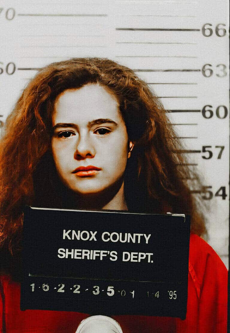Young woman with long curly hair facing the camera in a police booking photograph.