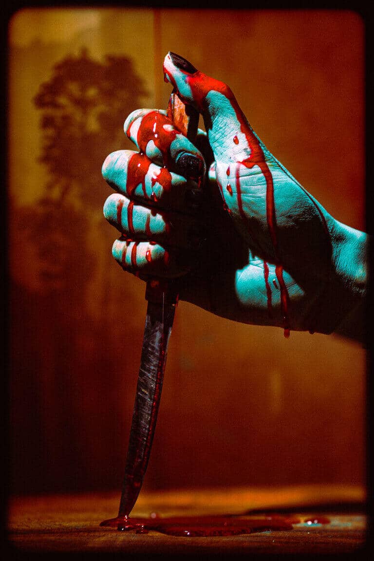 Close-up of a costumed hand with pale makeup holding a prop knife.