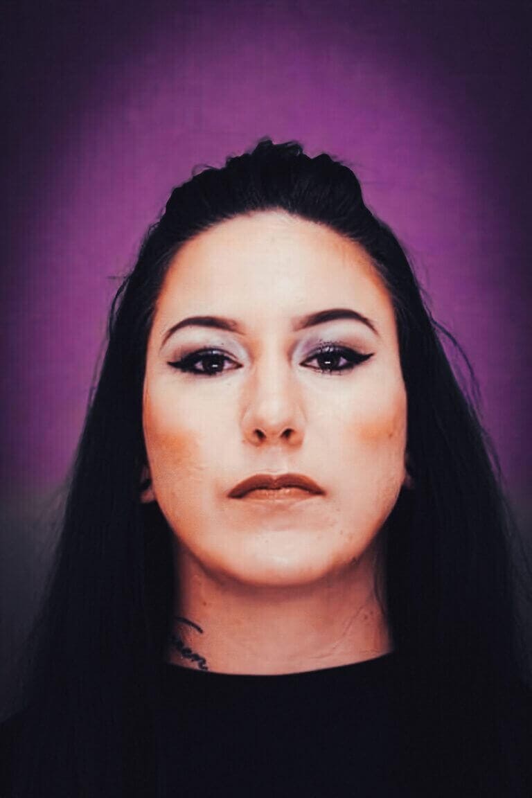 Portrait photograph of a dark-haired woman against a purple studio background.