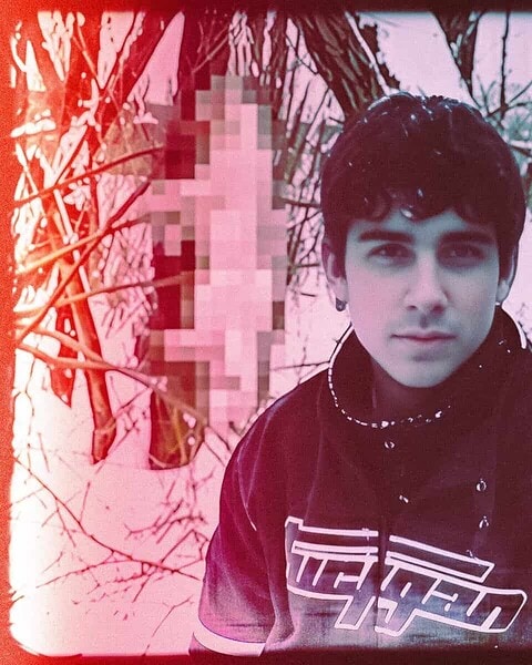 Two young men stand together in a bare winter woodland, with part of the frame pixelated.