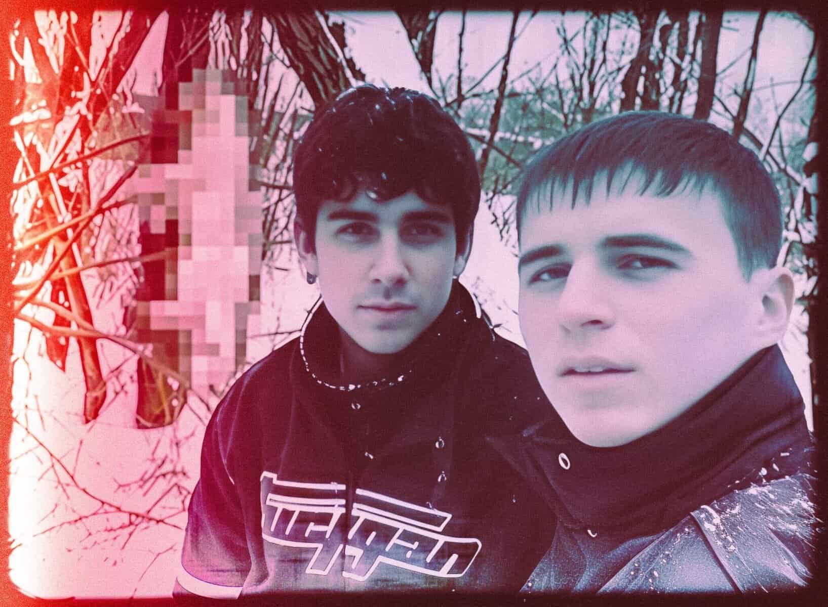 Two Young Men In A Dark, Eerie Forest With A Pixelated Object In The Background, Reflecting Human Darkness And Unsettling Themes.
