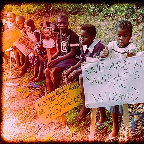Children protest for equality and justice, holding signs about witches, wizards, and societal issues in a rural environment.