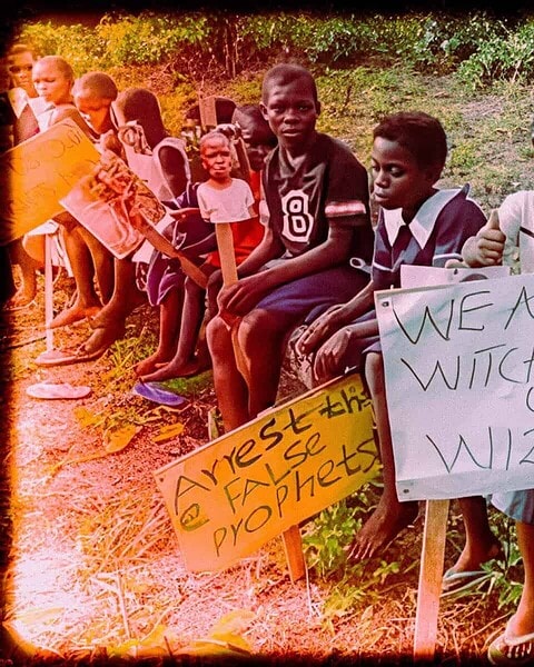 Children protest for equality and justice, holding signs about witches, wizards, and societal issues in a rural environment.