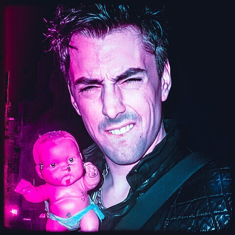 Eerie image of a man holding a disturbing doll with neon lighting.