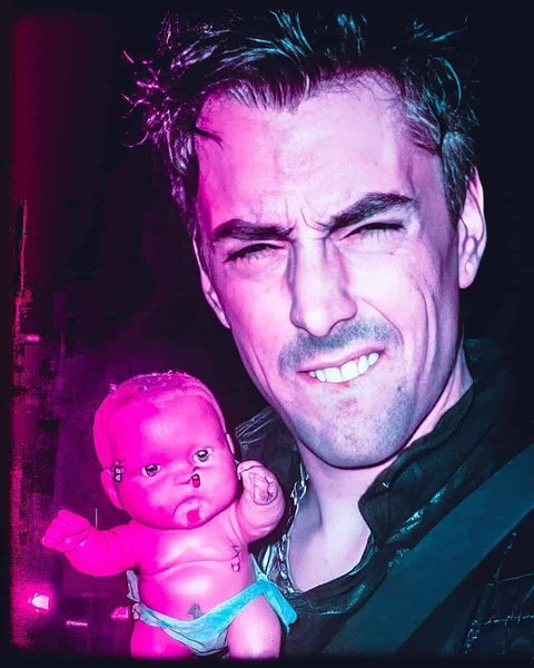 Eerie image of a man holding a disturbing doll with neon lighting.