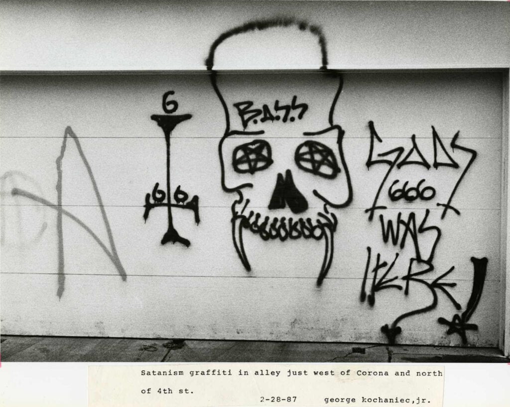 Black spray-paint graffiti on a light wall showing a skull with pentagram eyes, an inverted cross and the number 666.