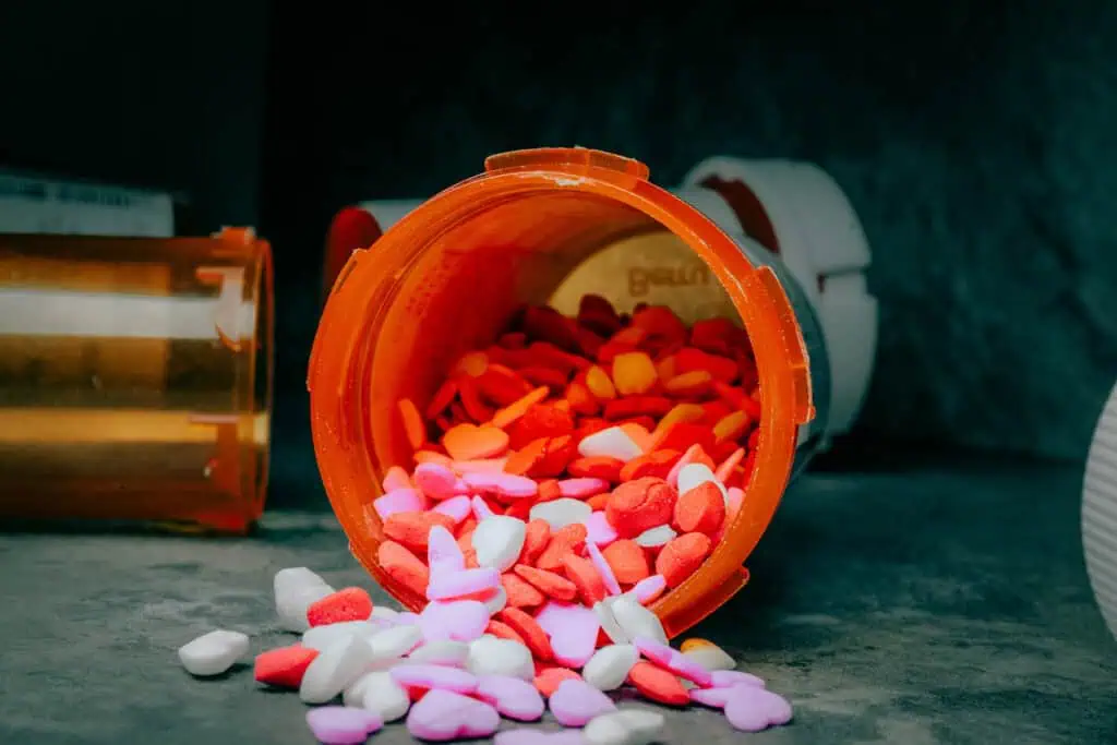 An orange prescription bottle lies on its side with red, pink and white pills spilling out.
