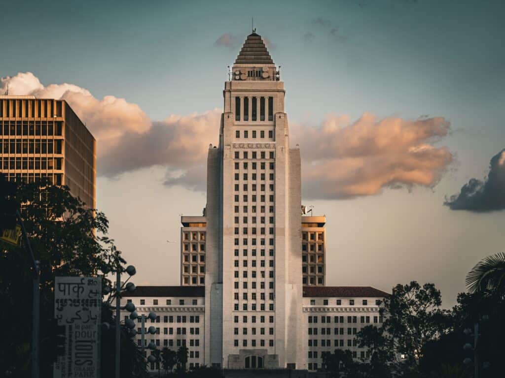 Iconic Los Angeles City Hall building during sunset with dramatic clouds.