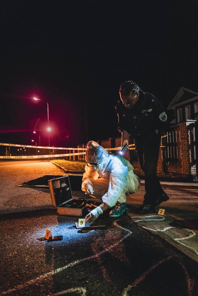 Police and forensic investigator examining a crime scene at night.