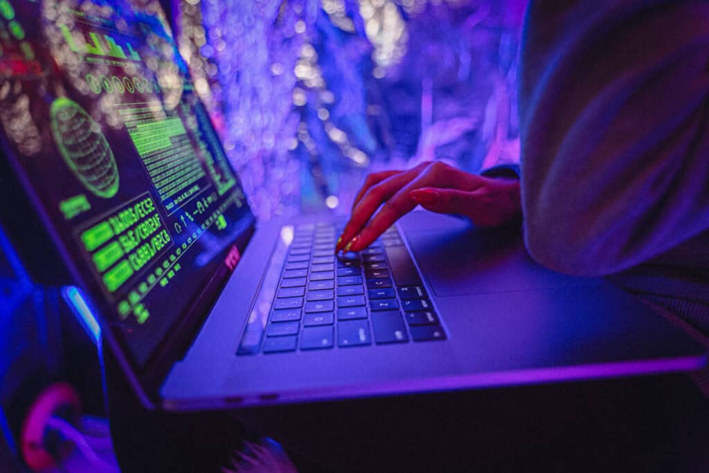 Person hacking on a laptop with dark web graphics and neon lights.