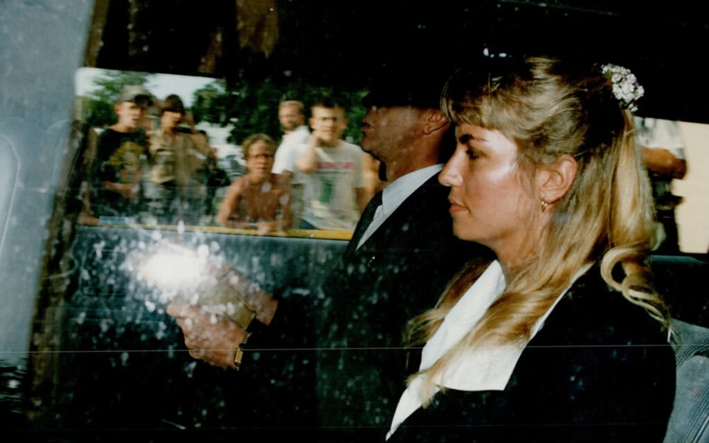People reflected in a car window during a public event.