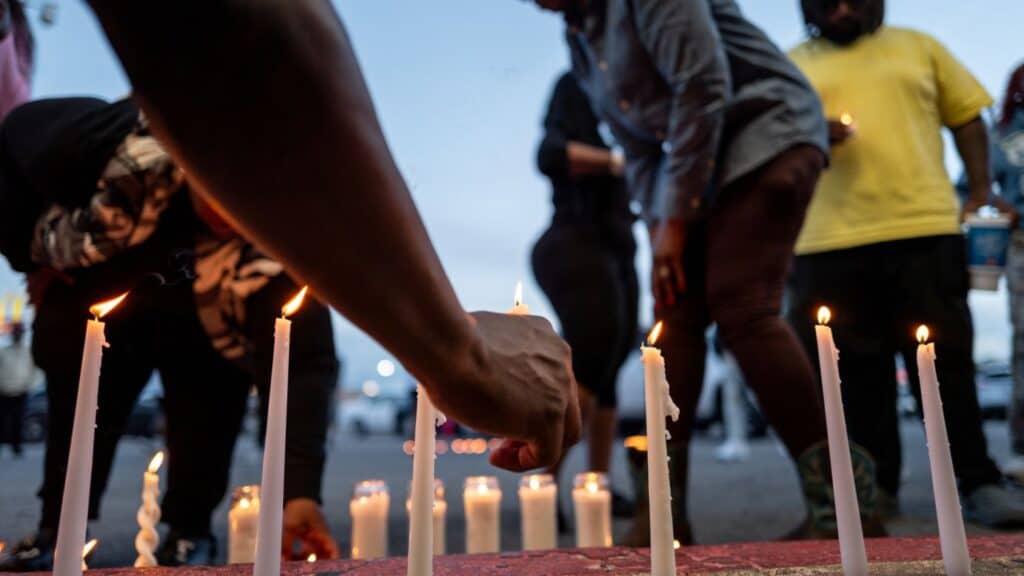 People lighting candles at an outdoor evening vigil.