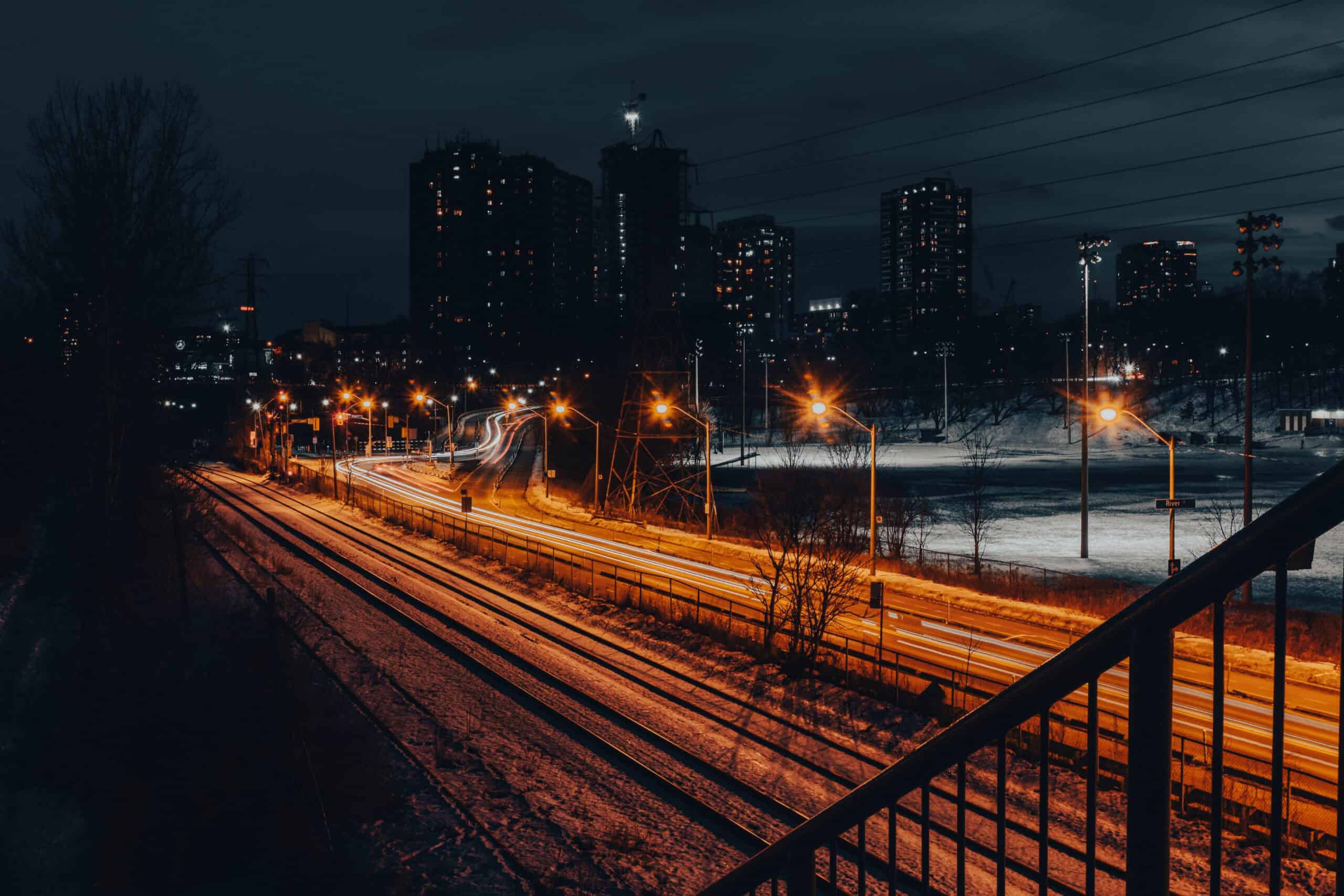 Nighttime cityscape with illuminated train tracks and high-rise buildings.