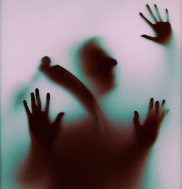 Silhouette of a person with hands pressed against a frosted glass panel, seen in pink and green light.