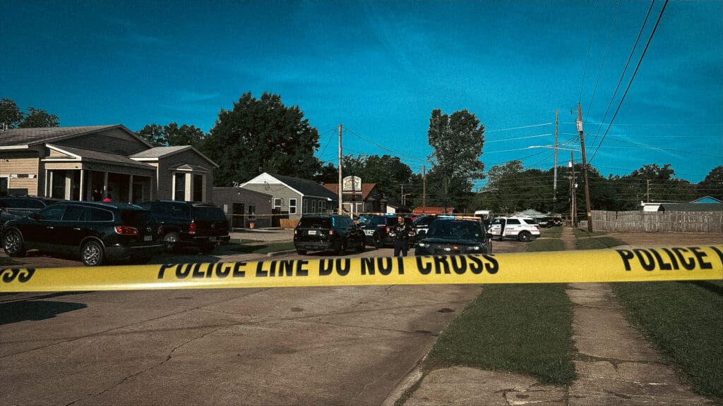 Yellow police tape across a residential street with patrol cars outside a house.