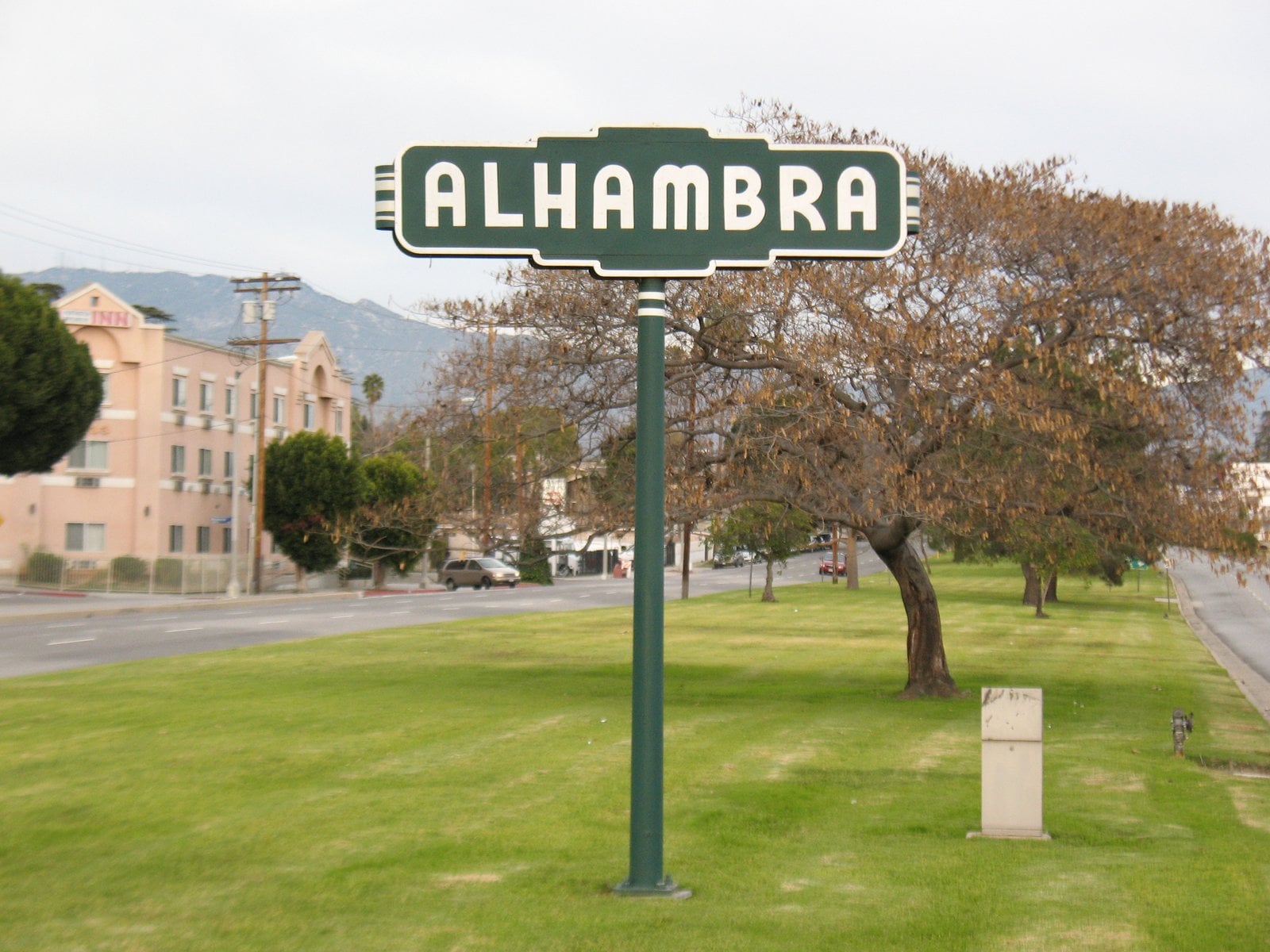 A city welcome sign reading Alhambra beside a road lined with trees and shrubs