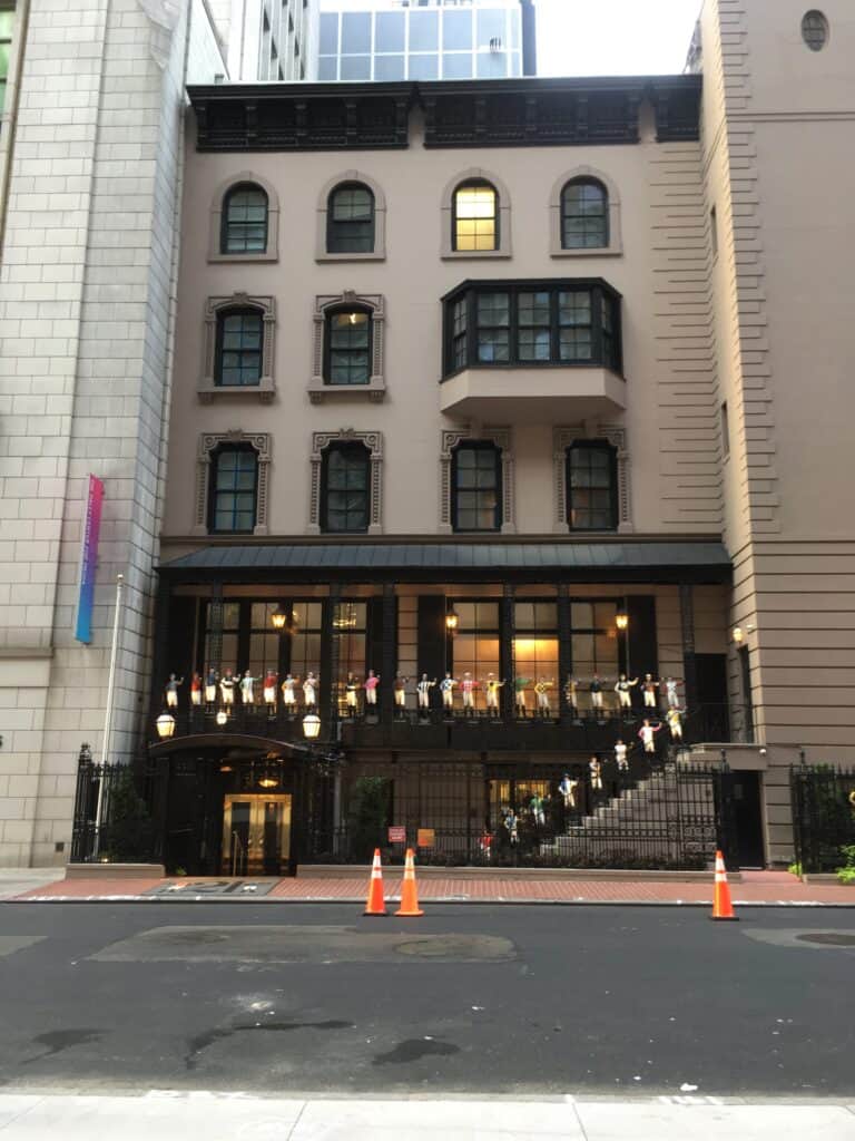 The four-story brownstone facade of the 21 Club on West 52nd Street in Manhattan, with a row of painted cast-iron jockey statues along the balcony railing above the entrance steps.