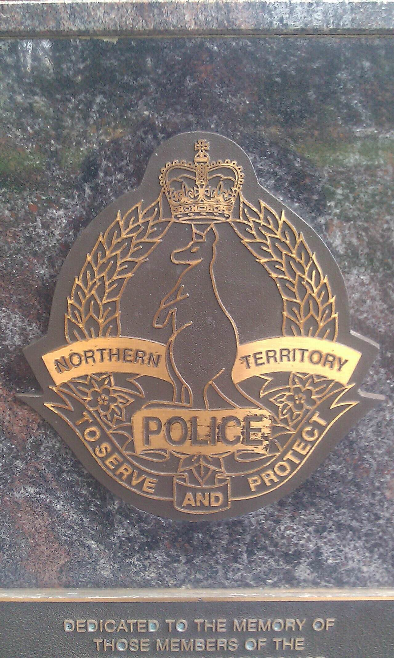 A metal, engraved plaque of the logo of the Northern Territory Police in Bicentennial Park in Darwin, Australia. depicting a kangaroo, a crown and the words Northern Territory Police and 'To Serve And…