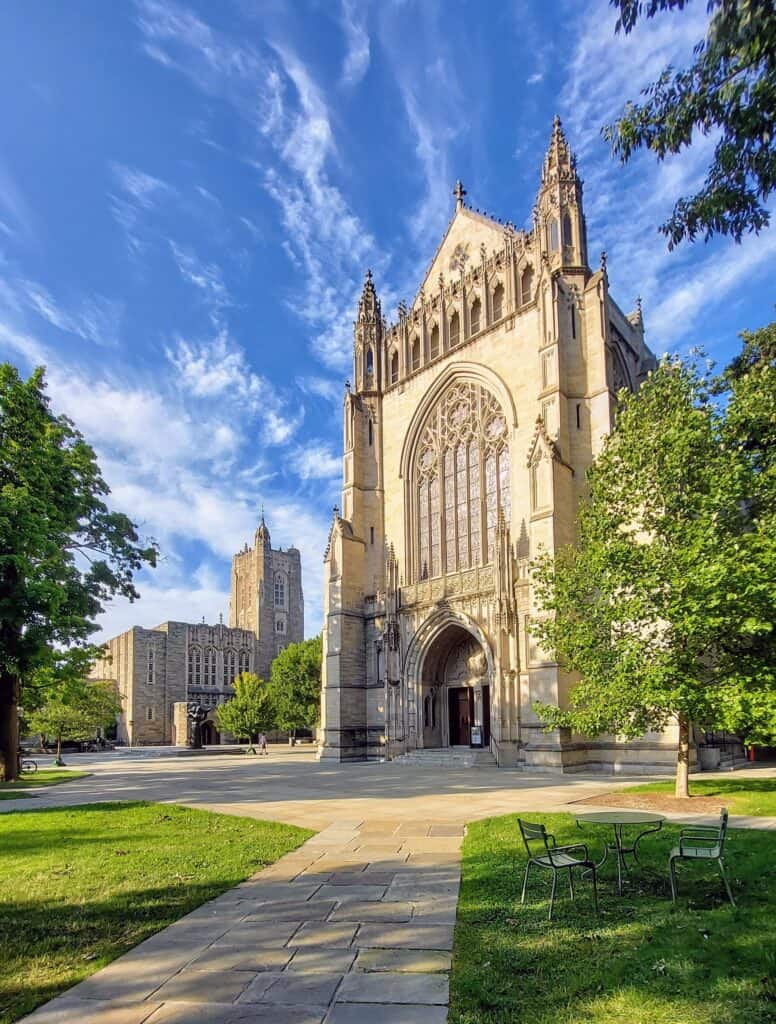 The Gothic stone tower and arched entrance of Princeton University Chapel on a sunny day, with lawns and trees in front.