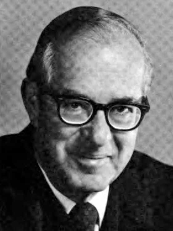 Black-and-white head-and-shoulders portrait of Justice Stanley Mosk, an older man with dark-rimmed glasses, a dark suit and tie, smiling slightly.