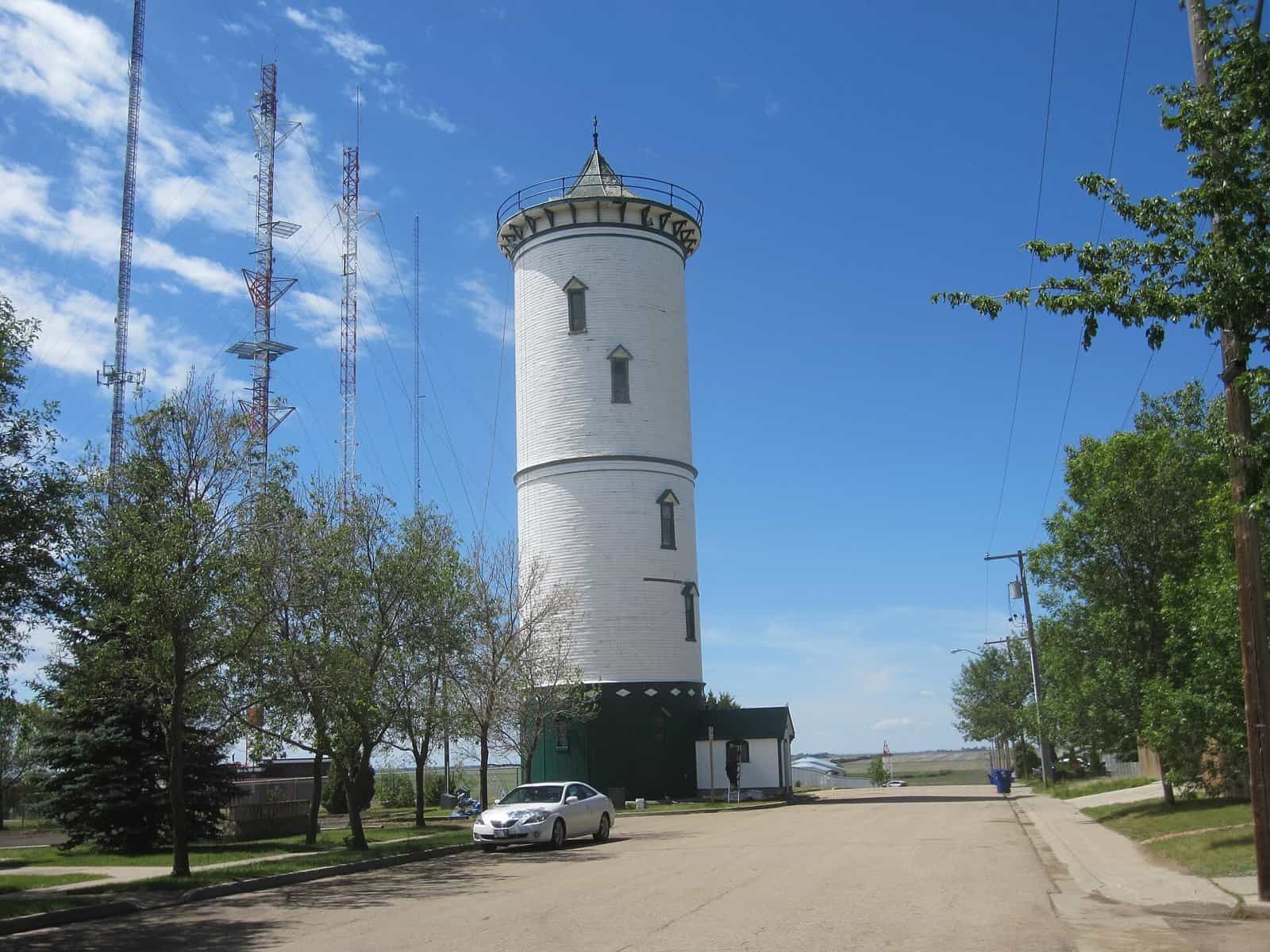 The white historic water tower on Signal Hill in Weyburn, Saskatchewan, beside radio masts under a blue sky