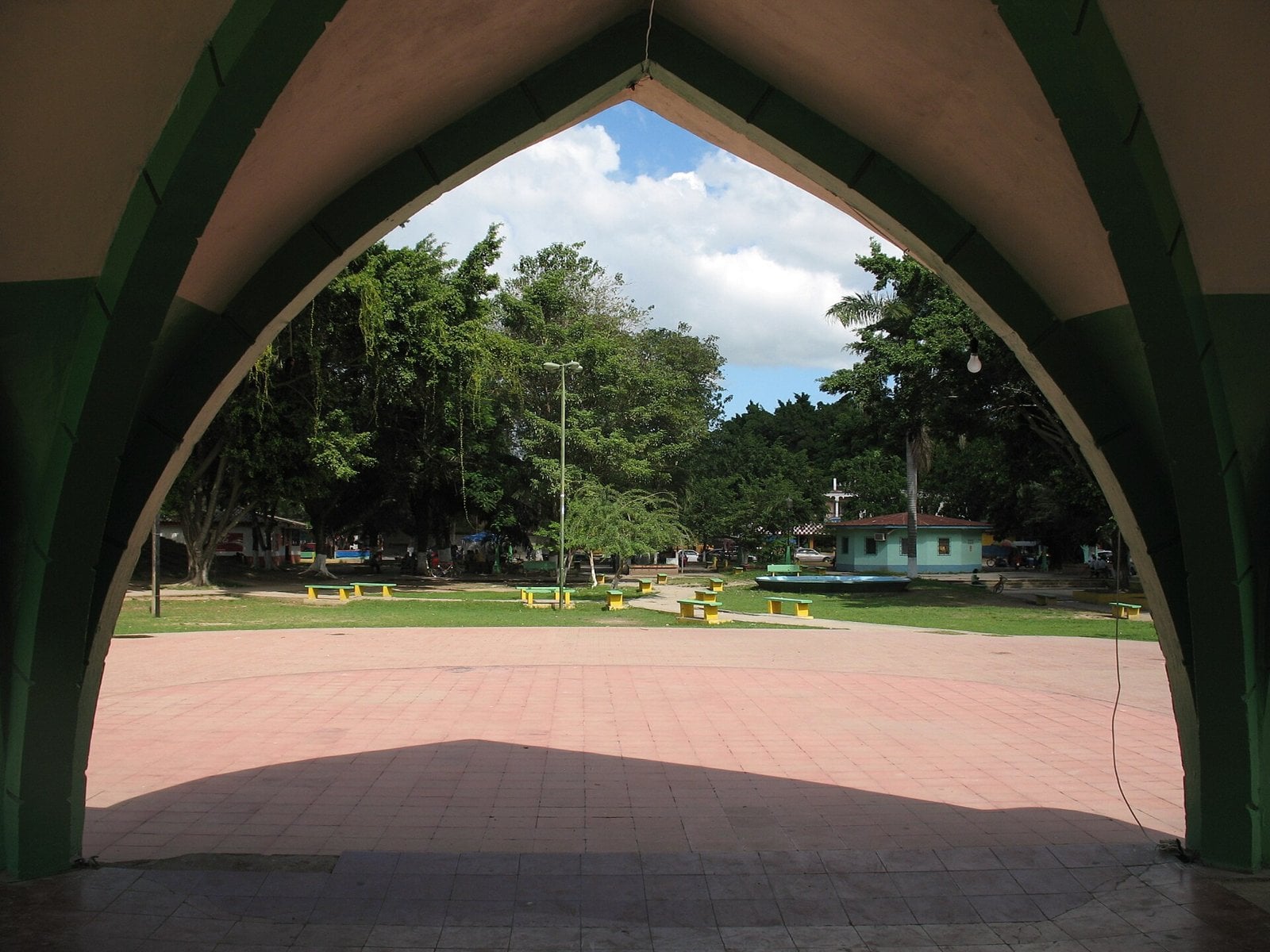 View through a green arched shelter onto the tree-lined central park of La Lima, Cortés, Honduras