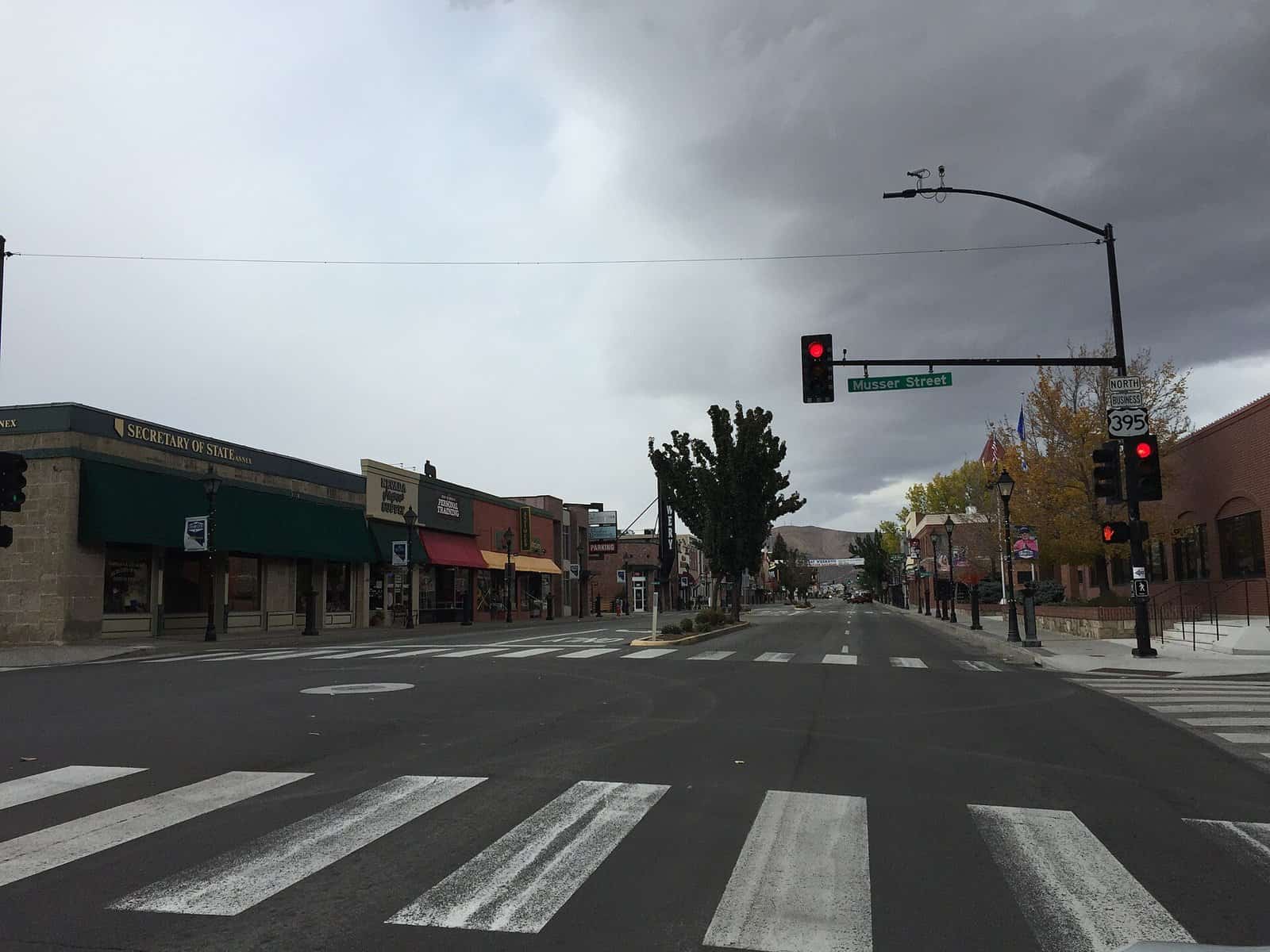 An empty crosswalk and storefronts looking north along Carson Street in downtown Carson City under gray clouds