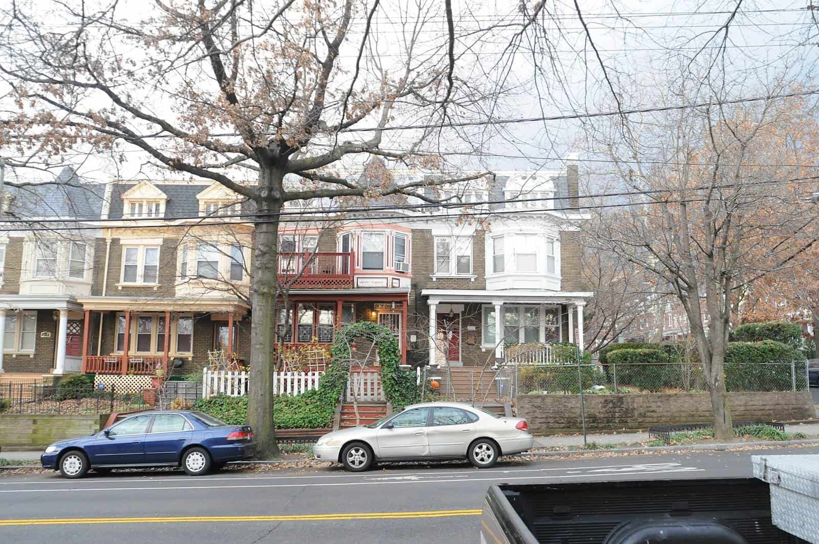A row of brick rowhouses with porches behind bare trees on a residential street in Columbia Heights, with parked cars at the curb