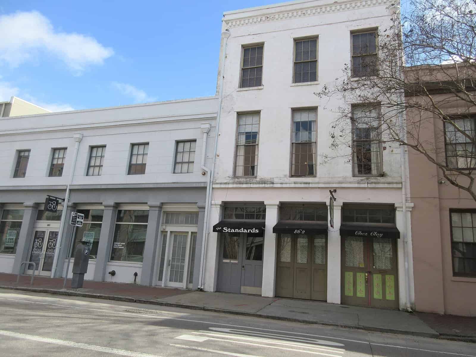 Two- and three-story historic commercial buildings with dark awnings along the sidewalk of Tchoupitoulas Street on a sunny day