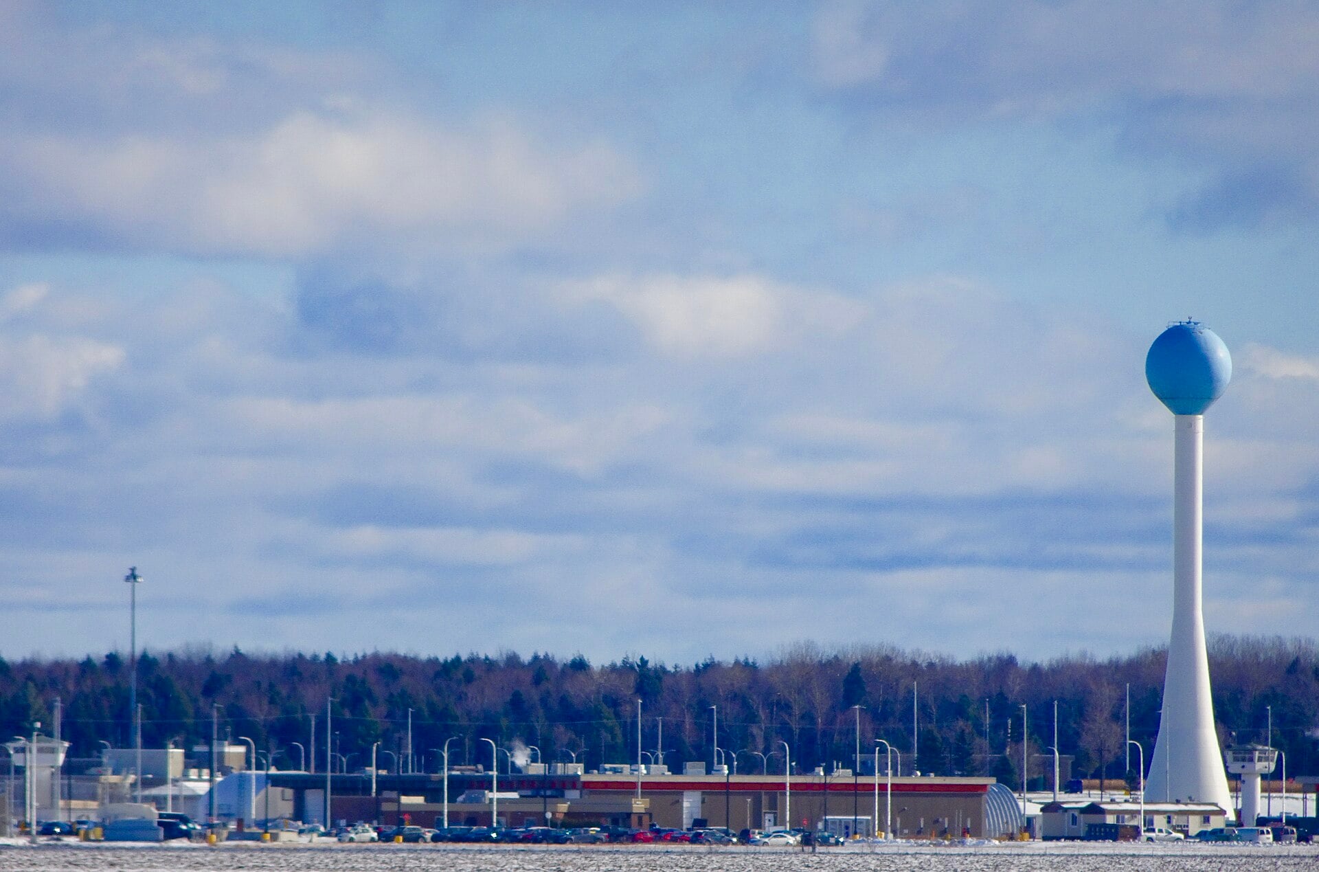 Low prison buildings and a tall white water tower with a blue top on flat snowy ground under a cloudy sky