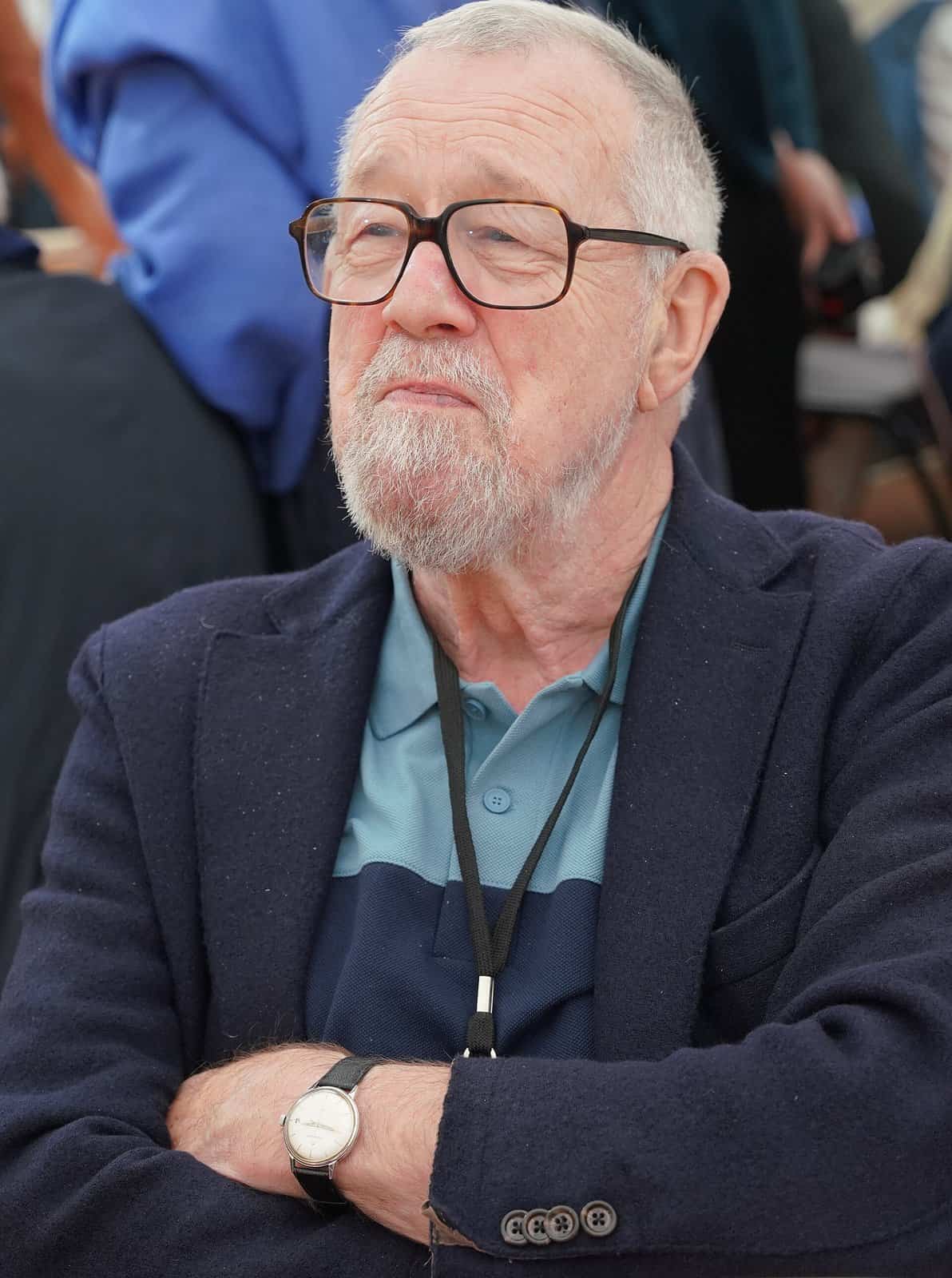 Gilbert Thiel, a white-haired man with glasses and a grey beard, photographed at a book fair in 2025.