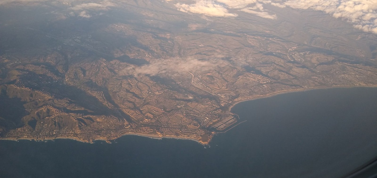 An aerial view of the Dana Point coastline in Orange County, with headlands, a harbor and hillside neighborhoods above the Pacific Ocean.