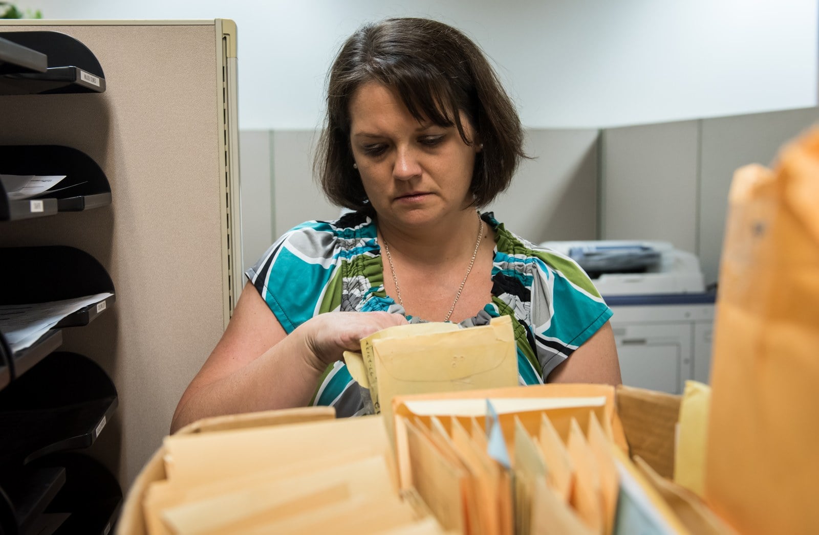 A woman with dark hair sorting through tightly packed manila case folders in an open file box on a desk.