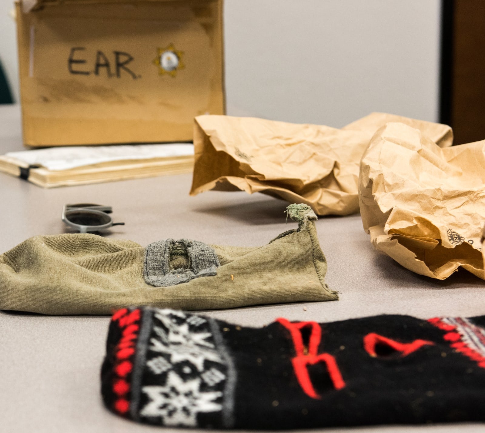 Two knitted ski masks, one black and red, lying on brown evidence paper beside evidence bags on a table.