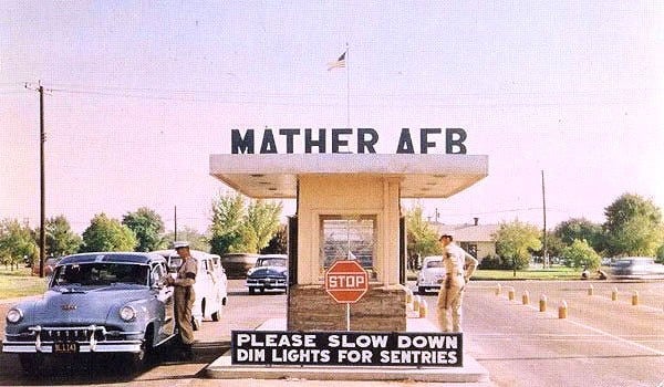 A vintage color photograph of the main gate of Mather Air Force Base, with a sign reading Mather AFB above a guard post and 1950s cars at the entrance.