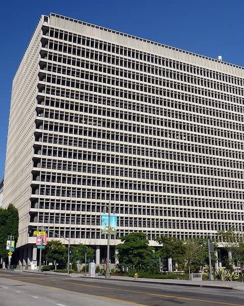 A tall modern office tower of stone and glass seen from the street, with a plaza in front