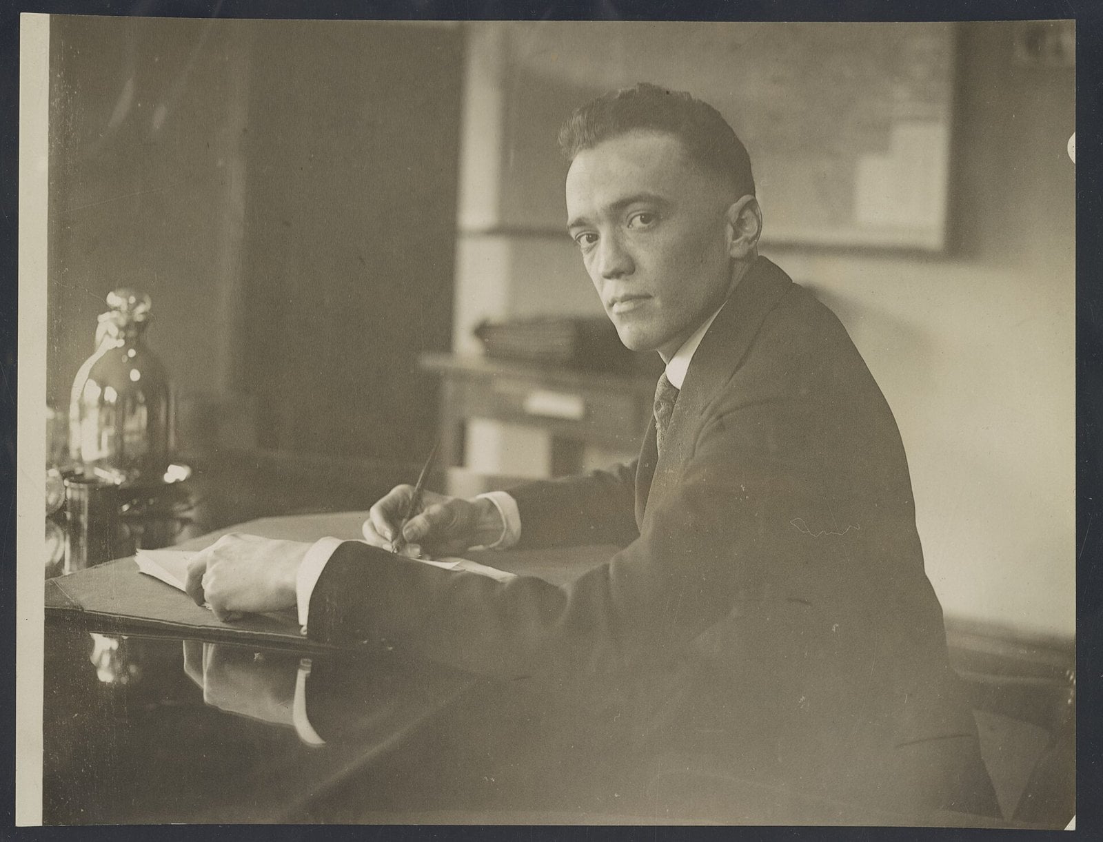 J. Edgar Hoover in a dark suit seated at a desk holding a pen, photographed in 1924