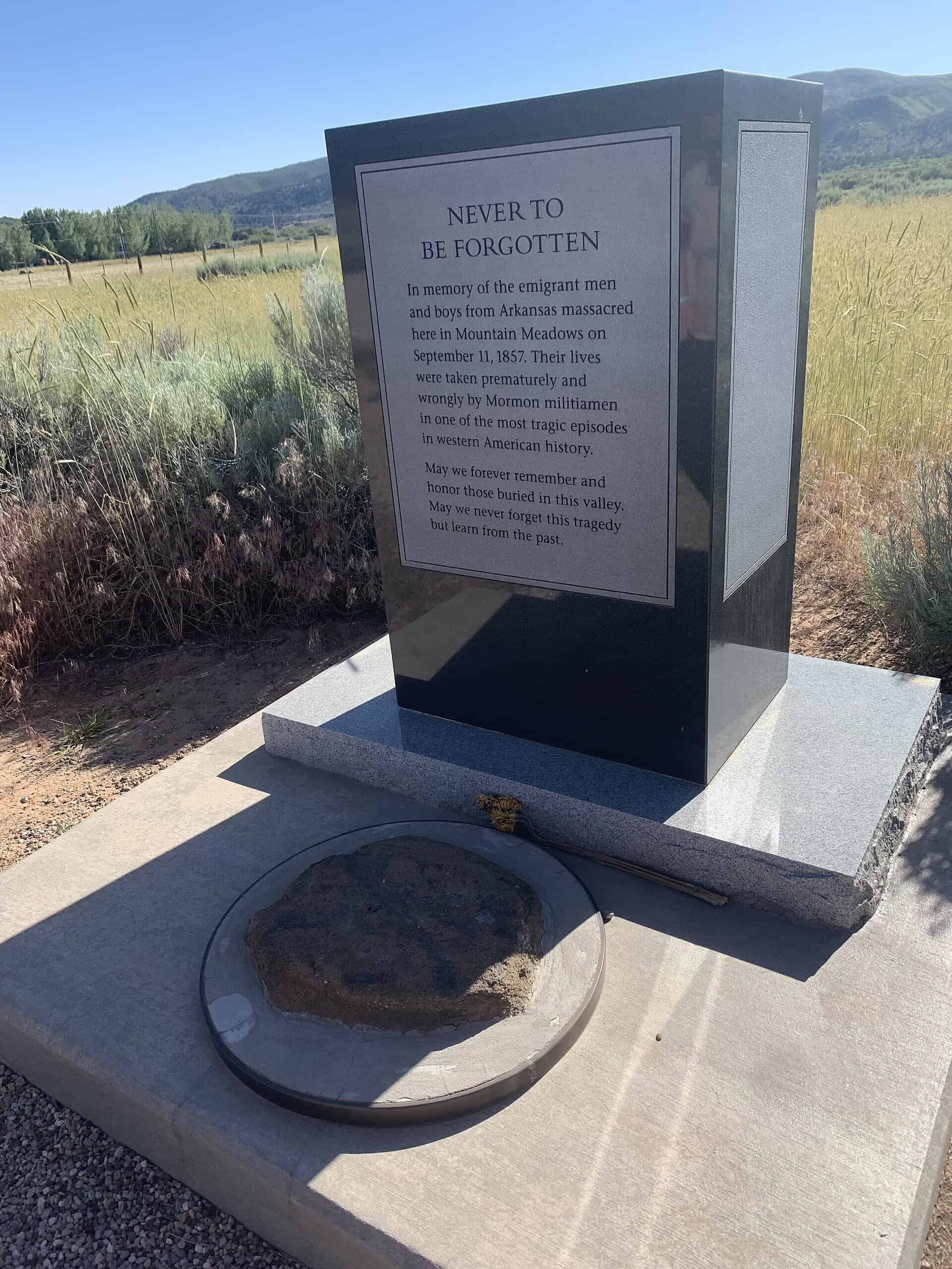 A black granite marker headed Never to be Forgotten on a concrete base, with a field and mountains behind it